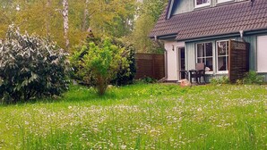 Ein zweistöckiges Haus mit überdachter Veranda, umgeben von einem üppigen Garten und hohen Bäumen.