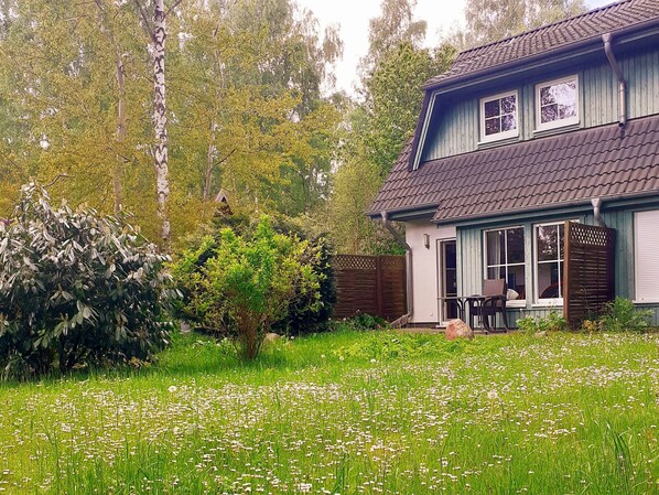 A two-story house with a covered porch, surrounded by a lush garden and tall trees.