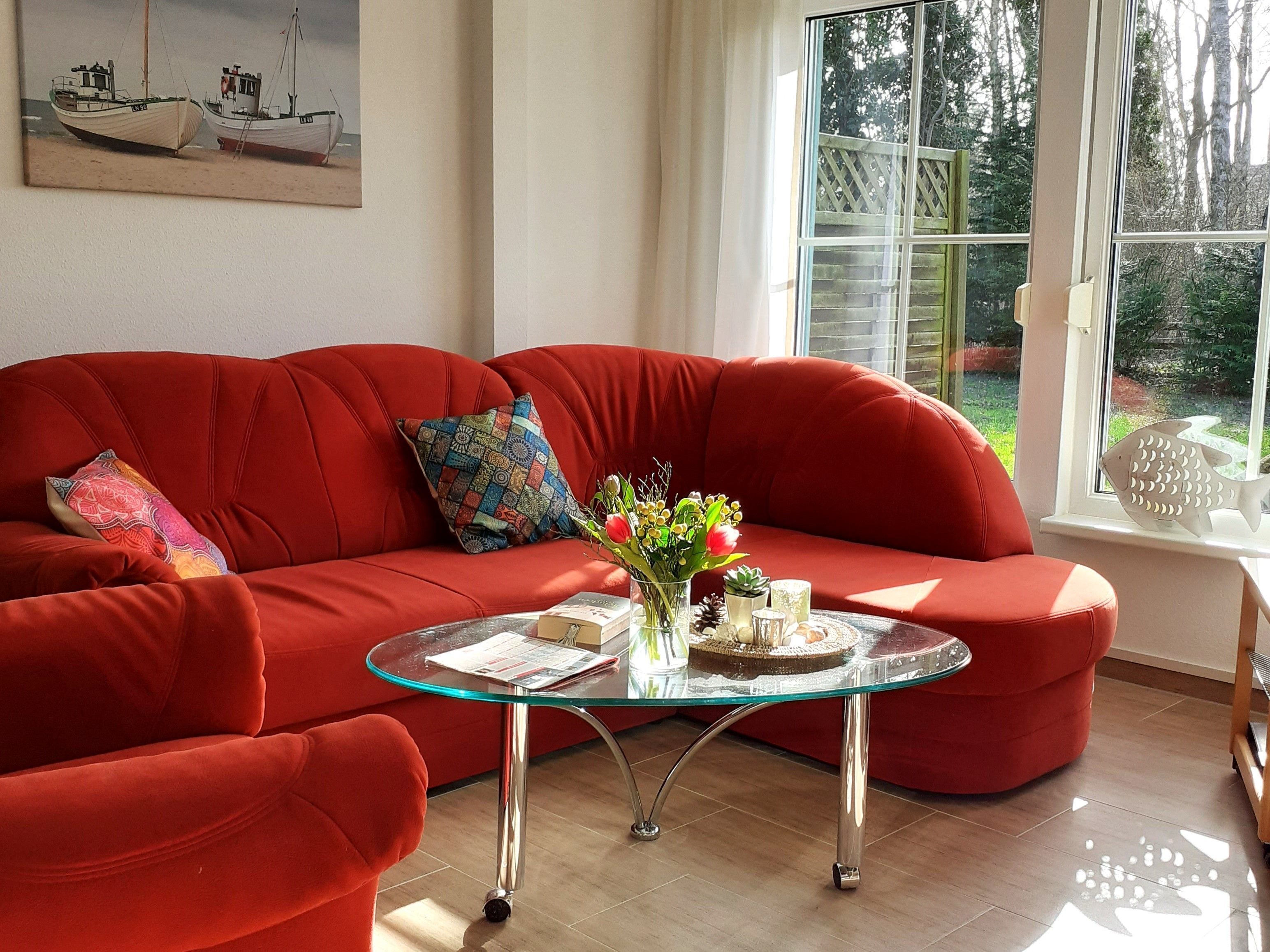 Ein rotes Sofa mit einem Glastisch in einem Raum mit einem großen Fenster, einem Bootsbild an der Wand und einer fischförmigen Dekoration auf der Fensterbank.