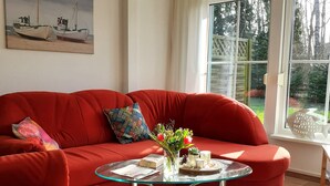 Ein rotes Sofa mit einem Glastisch in einem Raum mit einem großen Fenster, einem Bootsbild an der Wand und einer fischförmigen Dekoration auf der Fensterbank.