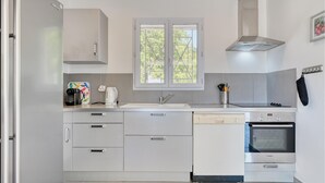 Cocina moderna con armarios blancos, lavavajillas Bosch, horno Siemens y ventana con vista a árboles.