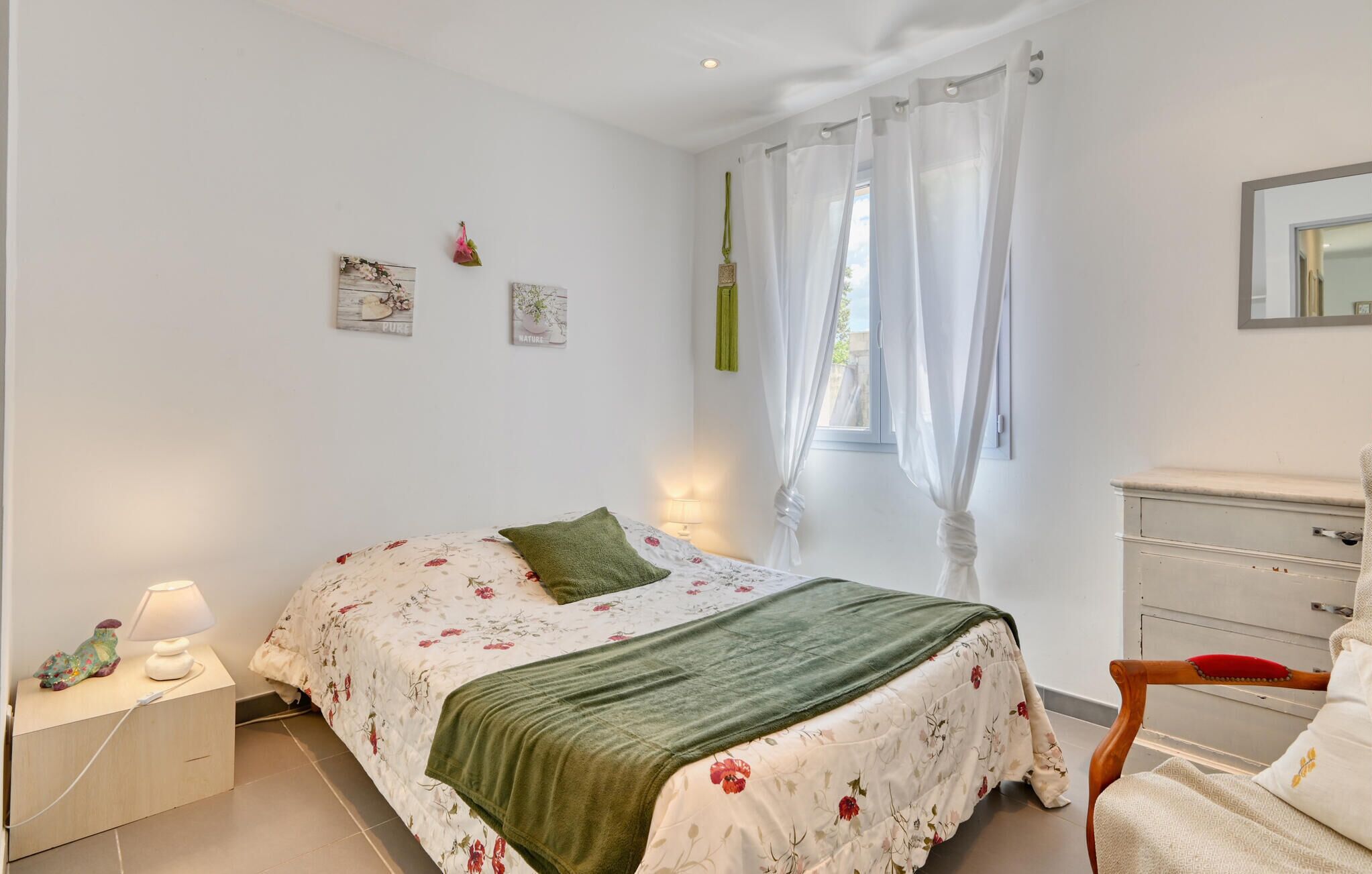 A bedroom with a bed, a nightstand, a dresser, and a window with curtains.