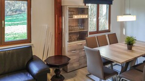 Un comedor con una mesa y sillas de madera, un mueble con puertas de vidrio y vistas a un paisaje verde a través de una ventana.