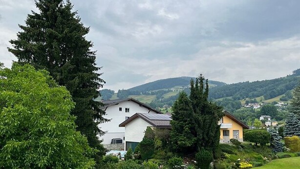 Un quartier résidentiel avec des maisons, un grand arbre et une colline en arrière-plan.