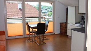 Une pièce comprenant une table et des chaises, un coin cuisine et une porte-fenêtre coulissante donnant sur un balcon.