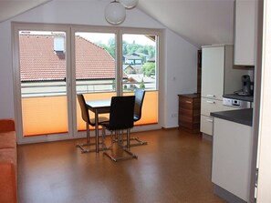Een kamer met een eettafel en stoelen, een kitchenette en een schuifpui naar een balkon.