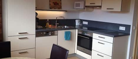 A compact kitchen with a microwave, stove, and sink. There is a dining table with chairs.