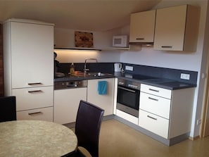 A compact kitchen with a microwave, stove, and sink. There is a dining table with chairs.