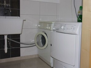 Een kleine wasruimte met een wasmachine, een gootsteen en een fles wasmiddel.