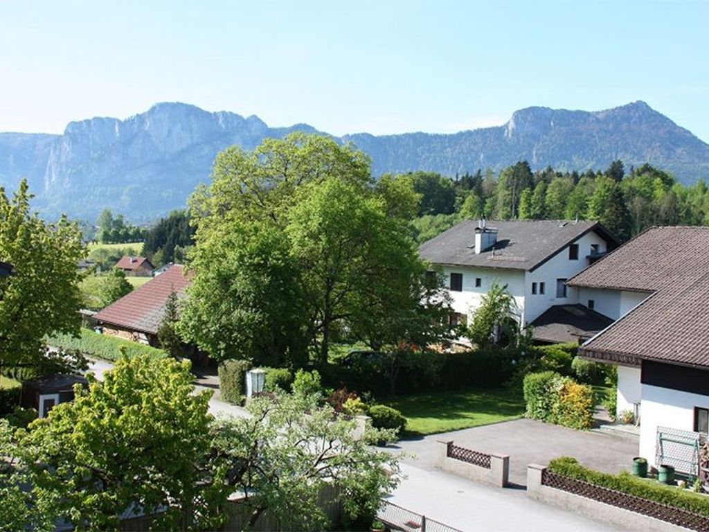 A residential area with houses, a large tree, and mountains in the background.