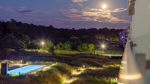 A nighttime view of a hotel with a swimming pool, illuminated pathways, and a forested backdrop. - Garden Suite Penthouse (Prora/Rügen)