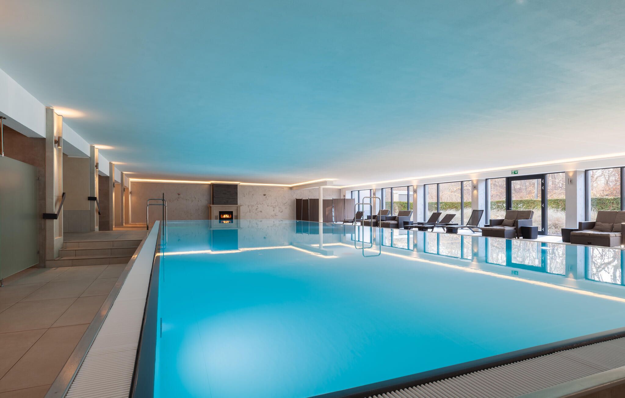 Una gran piscina interior con barrera de cristal, chimenea y zona de estar con tumbonas.
