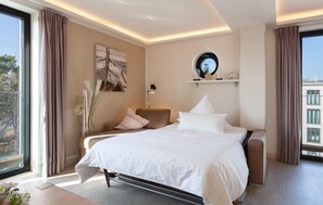 A modern bedroom with a large bed, a sofa, a wall-mounted shelf, and a window with curtains.