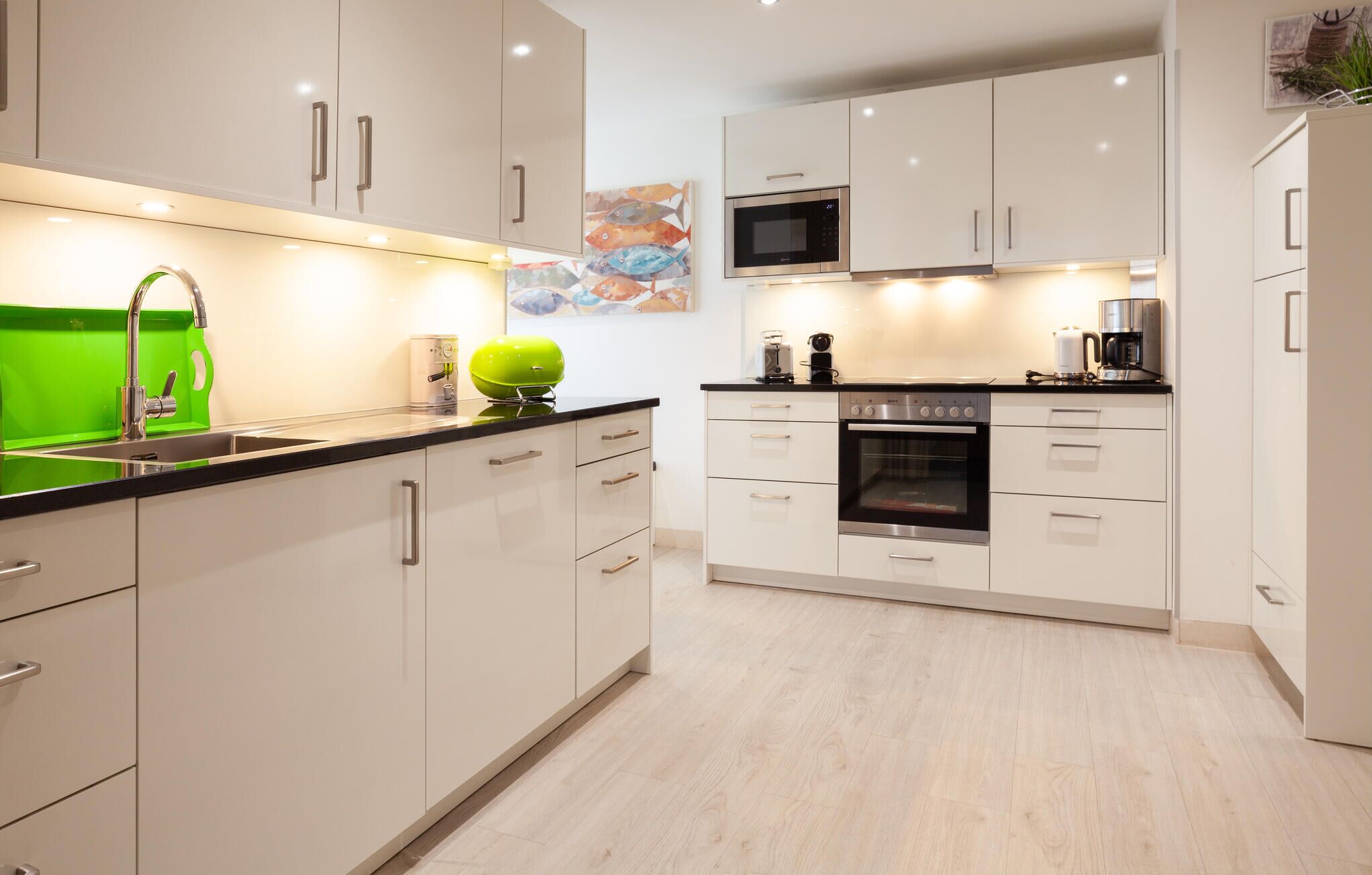 Eine moderne Küche mit weißen Schränken, einer schwarzen Arbeitsplatte, einer grünen Spüle und einem Bosch-Backofen.