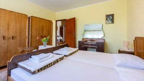 A hotel room with a large bed, wooden wardrobe, a desk with a lamp, and a mirror.