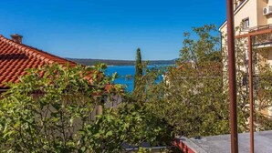 A coastal view with terracotta roofs, a clear blue sea, and lush greenery.