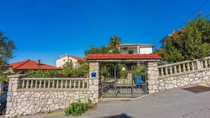 A stone-walled building with a red-tiled roof, a gated entrance, and a clear blue sky.