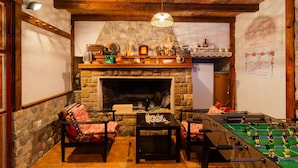 Una habitación acogedora con chimenea de piedra, vigas de madera, mesa de fútbol y mesa de ajedrez.