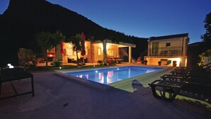 Una piscina con sillas de descanso, un área de estar techada y un edificio con una escalera.