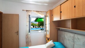 Un dormitorio con cama, armario de madera y ventana con vistas a una piscina y follaje.