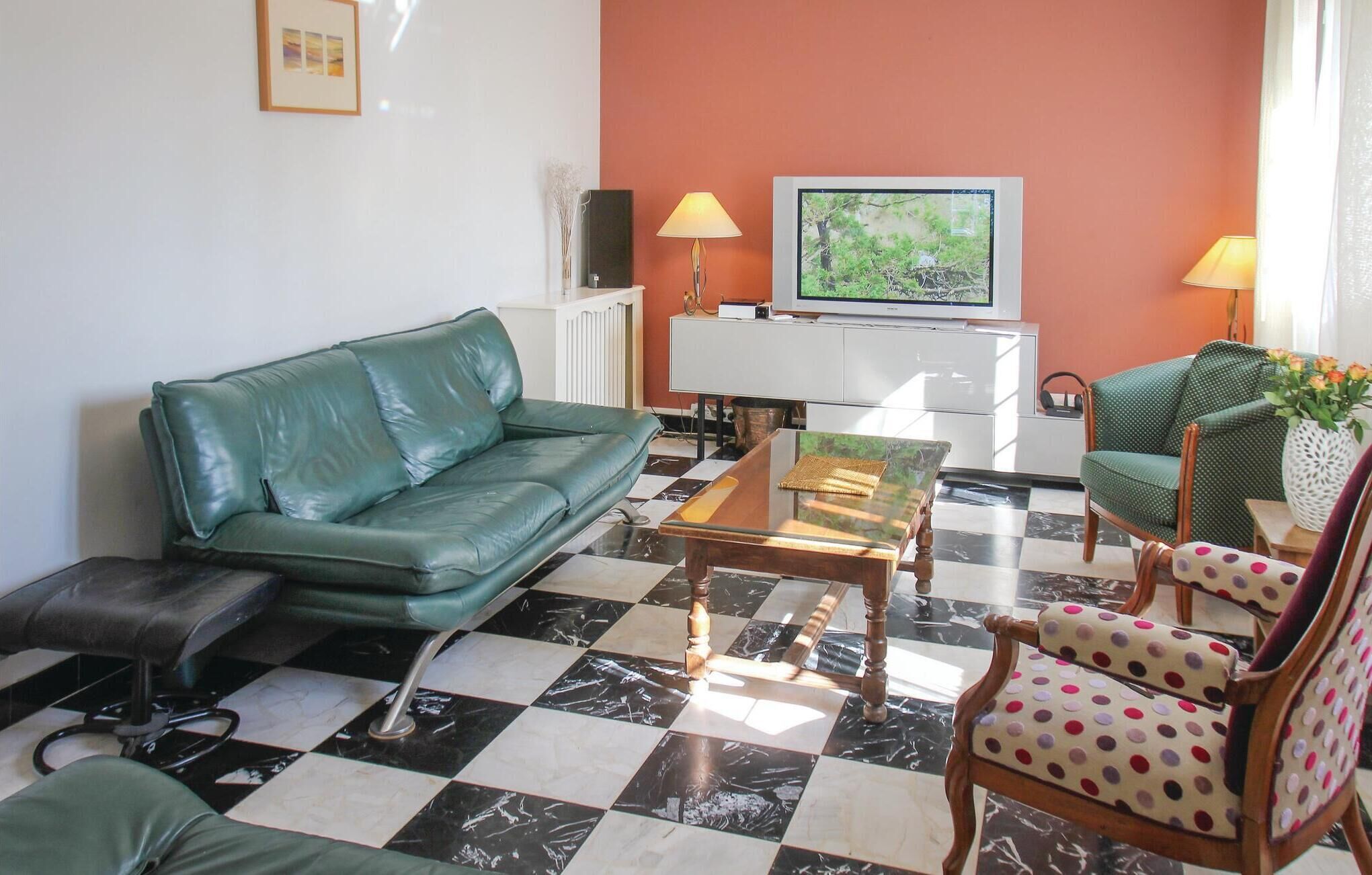 A living room with a green sofa, a coffee table, a patterned armchair, and a television against an orange wall.