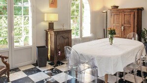 A dining area with a checkered floor, clear chairs, a white tablecloth-covered table, and a wooden cabinet with a lamp on it. - Lovely home in Montélimar (Montélimar)