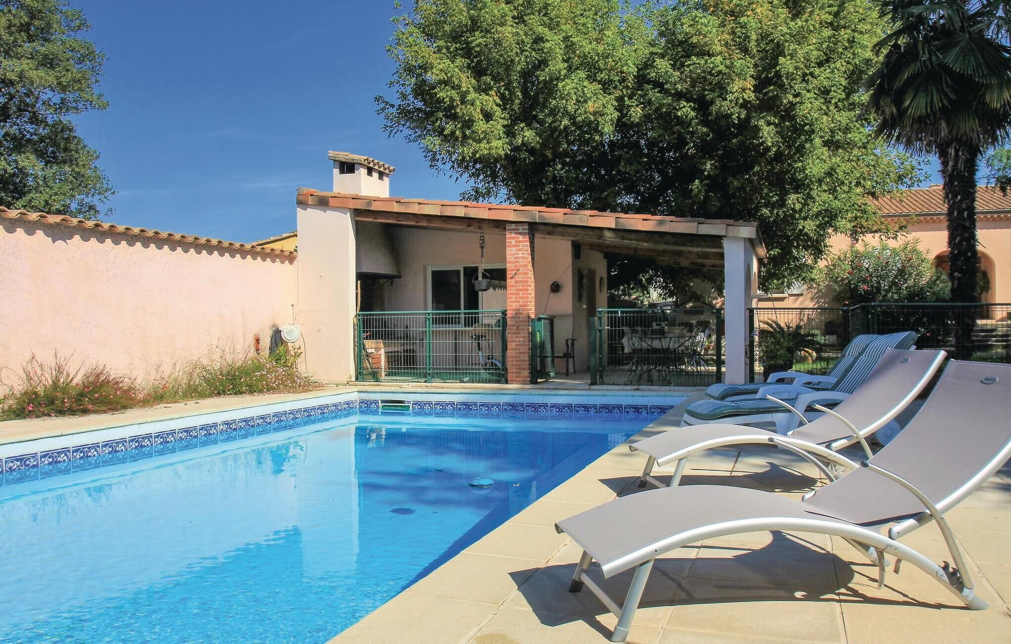 A swimming pool with lounge chairs, a covered patio, and a building with a tiled roof.