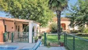 A pool area with lounge chairs, a fenced patio, and a building with arches and a tiled roof. - Lovely home in Montélimar (Montélimar)