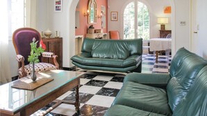 A living room with a green leather sofa, a glass coffee table, and a polka-dotted chair. There is a checkered floor and a dining area in the background. - Lovely home in Montélimar (Montélimar)