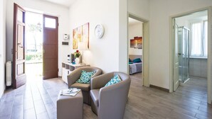 A modern living room with a sofa, ottoman, and a coffee table. There is a wall clock and a painting. The room has a wooden floor and a glass door leading to a balcony. - Awesome home in Massa (MS) with WiFi (Massa (MS))
