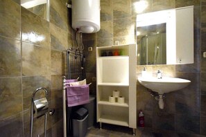 Un baño con ducha, lavabo, espejo y repisas con artículos de aseo.