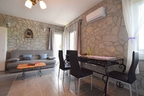 Una sala de estar con pared de piedra, un sofá, una mesa de centro y un comedor con sillas y una mesa.