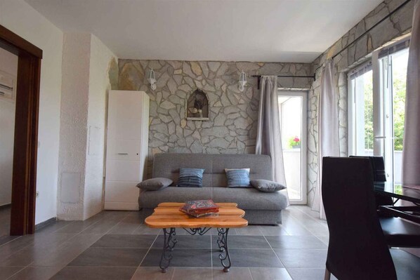 A living room with a stone wall, a sofa with cushions, a wooden coffee table with a book, and a piano.