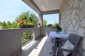 A balcony with a table and chairs, potted plants, and a stone wall.