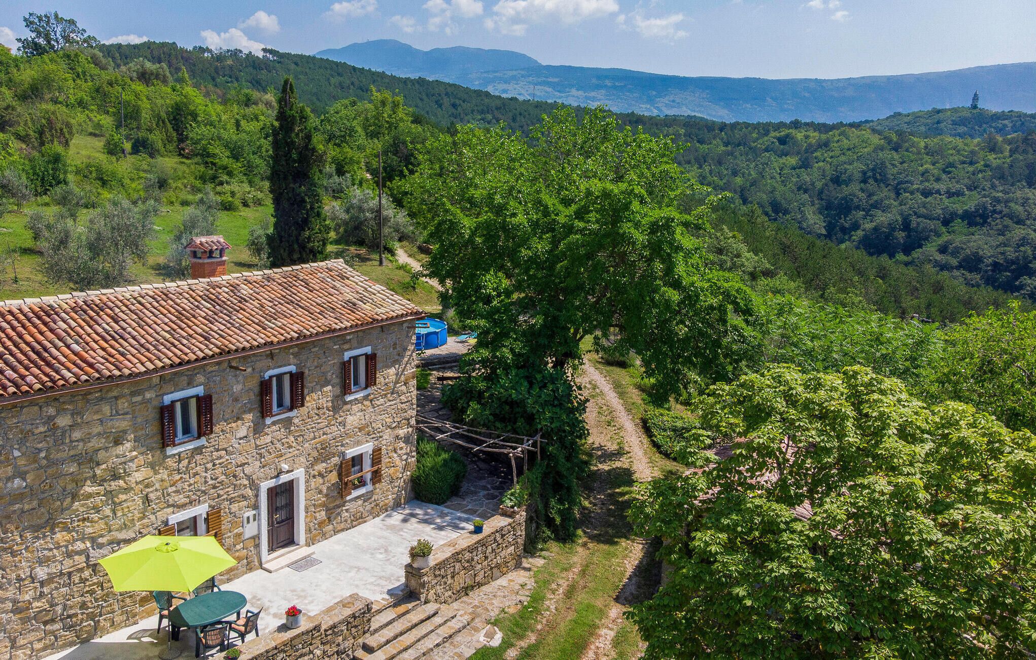 A stone building with a tiled roof, a patio with a table and chairs, and a view of a lush valley.