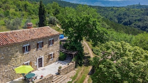 A stone building with a tiled roof, a patio with a table and chairs, and a view of a lush valley. - Nice home in Skabici with WiFi (Skabici)