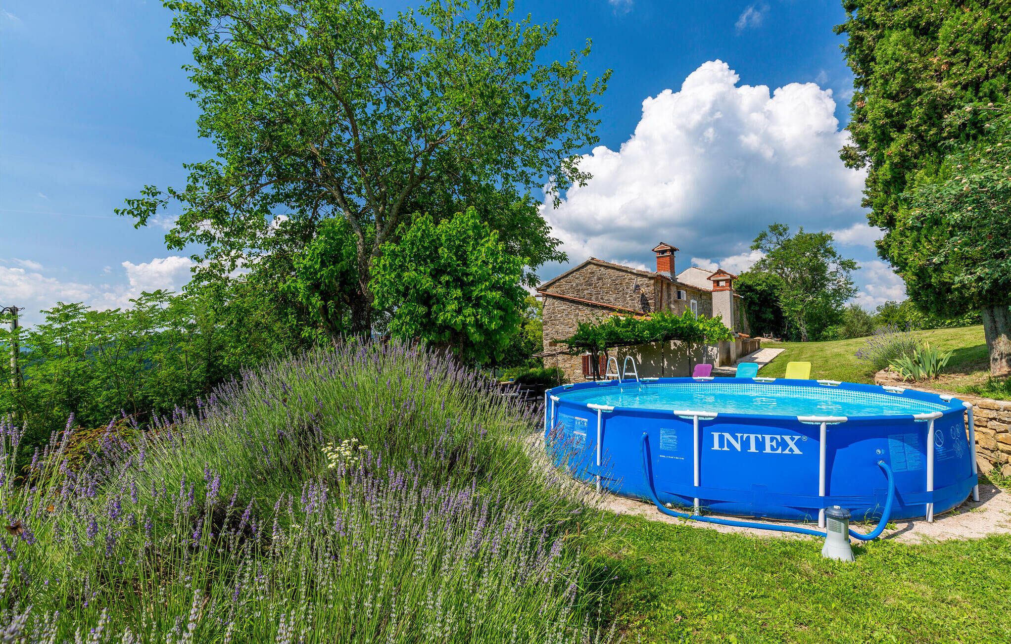 Uma piscina inflável azul da marca INTEX com uma casa de pedra ao fundo.