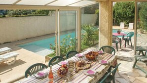 An outdoor dining area with a pool view, a table set for two with plates, glasses, and a bottle of wine. - Amazing home in Milhaud with WiFi (Milhaud)