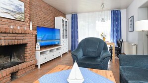 Een woonkamer met een open haard van baksteen, een televisie, een blauw tapijt met patroon en een modelzeilboot.
