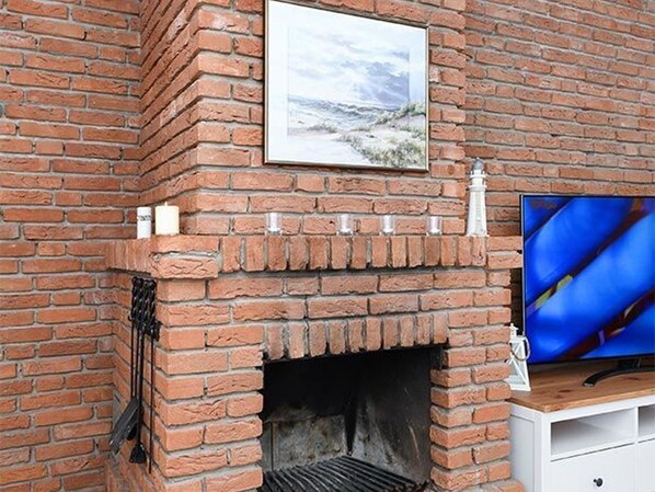 Een bakstenen openhaard met daarboven een lijstwerkfoto, een televisie op een houten standaard rechts en een witte kast eronder.