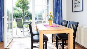 Een eetgedeelte met een houten tafel, zwarte stoelen en een gele vaas met bloemen.