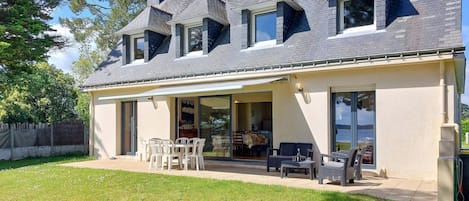 Una casa con porche cubierto, amplias ventanas y jardín con césped.