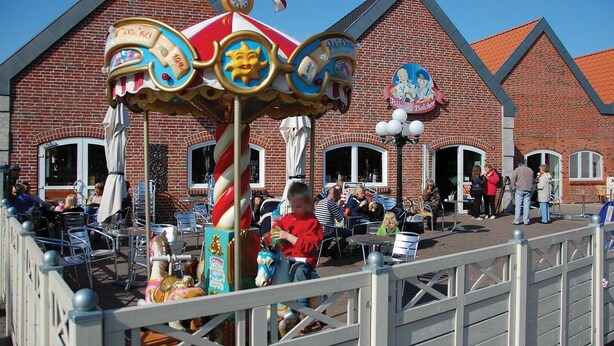 A carousel with a candy cane, a building with a red roof, and people sitting at tables outside. - Gorgeous home in Blåvand with sauna (Blåvand)