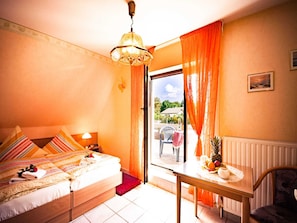 Ein Schlafzimmer mit einem Bett, einem Tisch mit Obst, einem Stuhl, einem Fenster mit Vorhängen und Blick ins Freie.