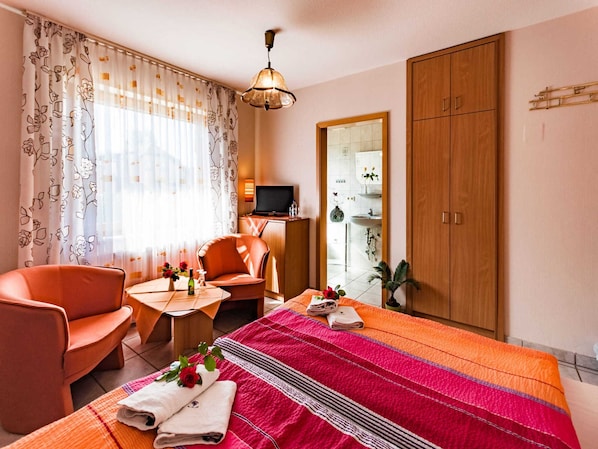 A hotel room with a bed, a sofa, a TV, a desk, and a wardrobe.