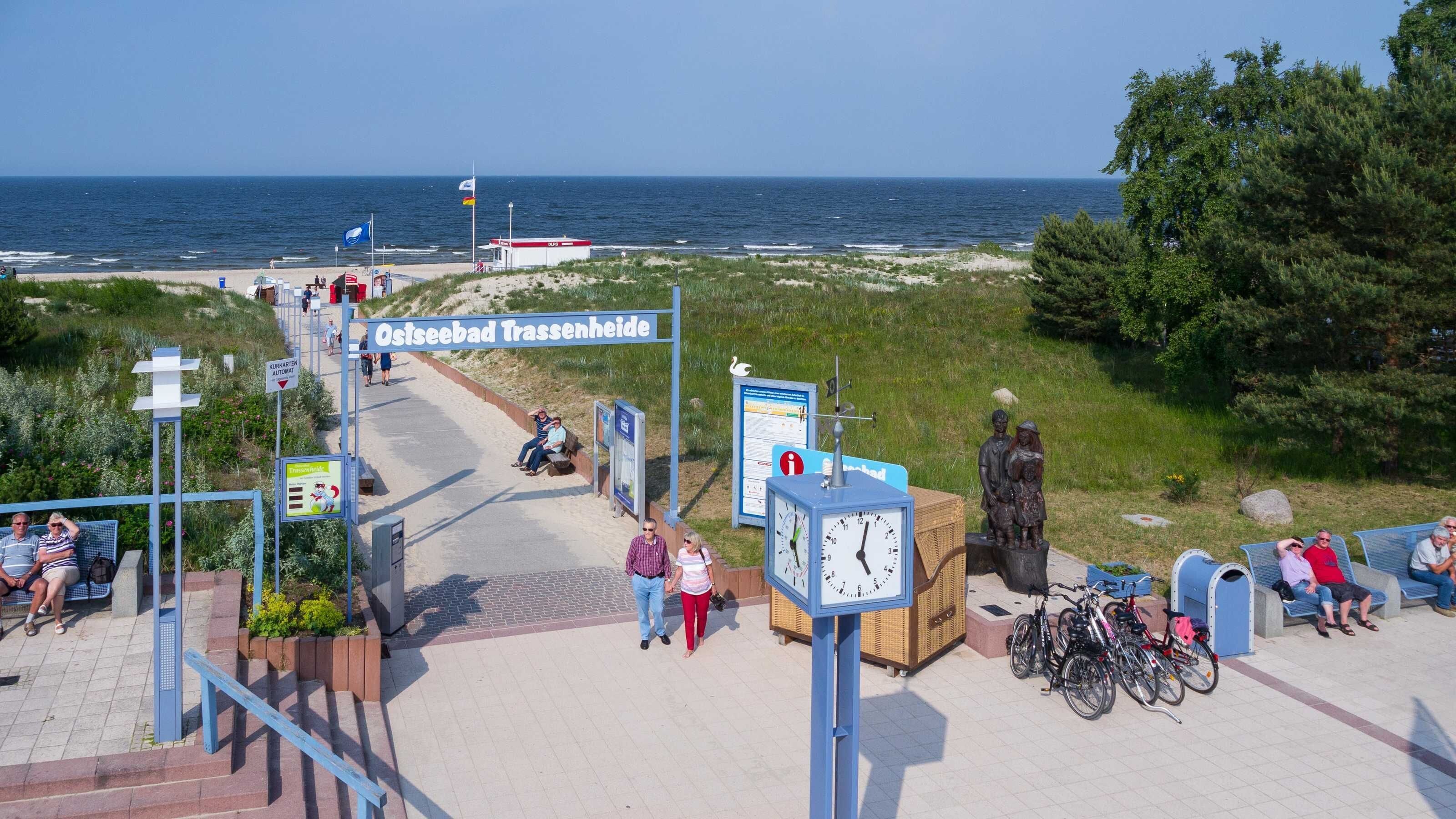 Ein Küstenweg mit Bänken, einer Uhr und einer Statue.