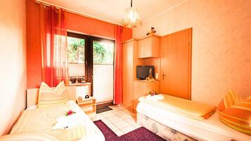 A room with two beds, a television, a desk, and a window with curtains.