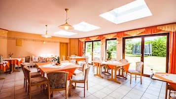 Ein Essbereich mit Tischen und Stühlen, großen Fenstern und einer Decke mit Oberlichtern.