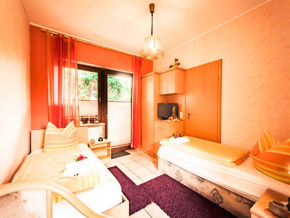 A room with two beds, a television, a desk, and a window with curtains.