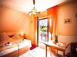 Ein Schlafzimmer mit einem Bett, einem Tisch mit Obst, einem Stuhl, einem Fenster mit Vorhängen und Blick ins Freie.